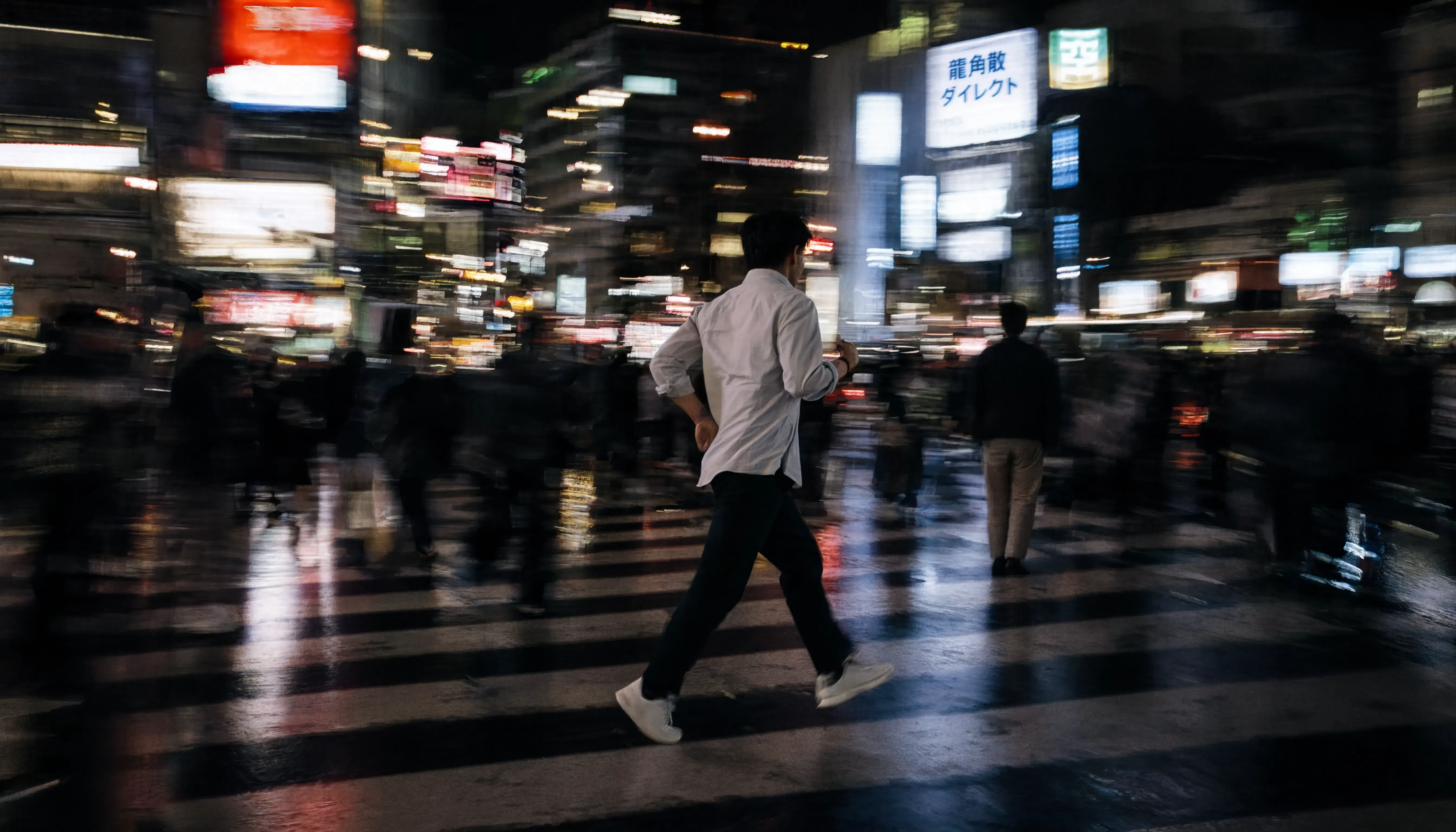 A person running across a rainy street at night with motion blur